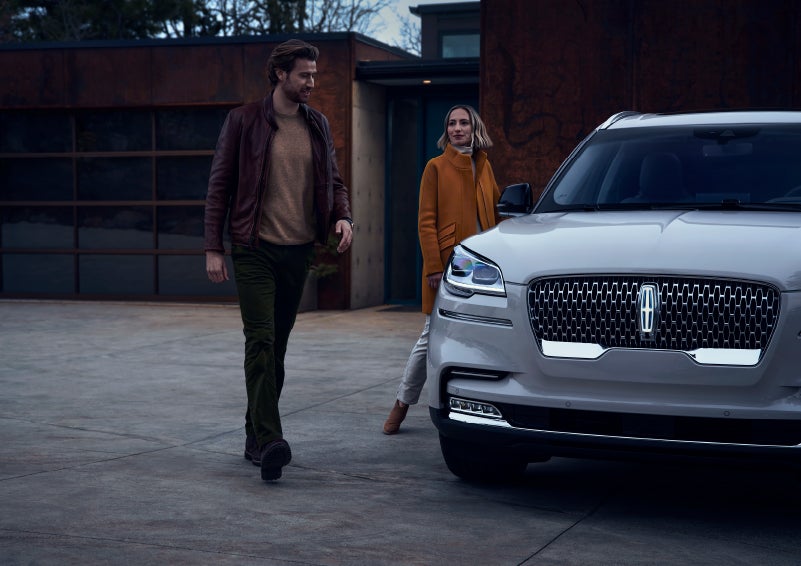 A man and a woman approaching a 2024 Lincoln Aviator® SUV, which illuminates certain lights when they are close | LaFontaine Lincoln Flushing in Flushing MI