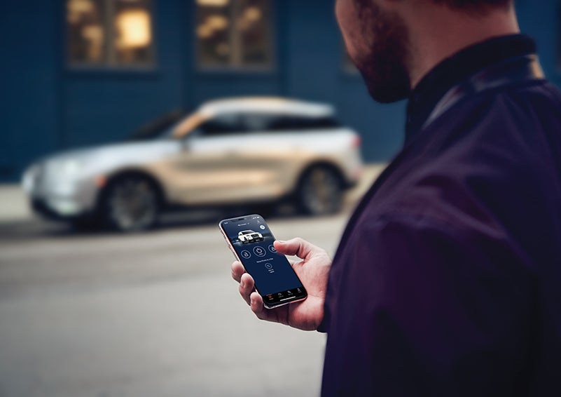 A person is shown interacting with a smartphone to connect to a Lincoln vehicle across the street. | LaFontaine Lincoln Flushing in Flushing MI