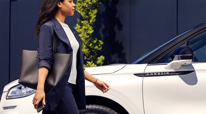 A woman approaches a 2024 Lincoln Corsair® SUV while holding a smartphone. | LaFontaine Lincoln Grand Blanc in Flint MI