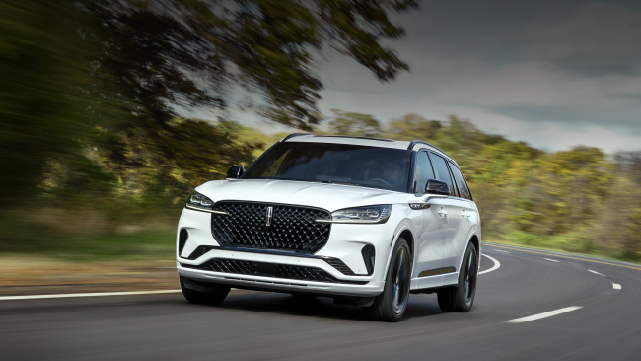 A white 2025 Lincoln Aviator® SUV is being driven down a road lined with trees. | LaFontaine Lincoln Grand Blanc in Flint MI