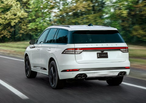 A white 2026 Lincoln Aviator® SUV is being driven away down a road lined with colorful trees. | LaFontaine Lincoln Grand Blanc in Flint MI