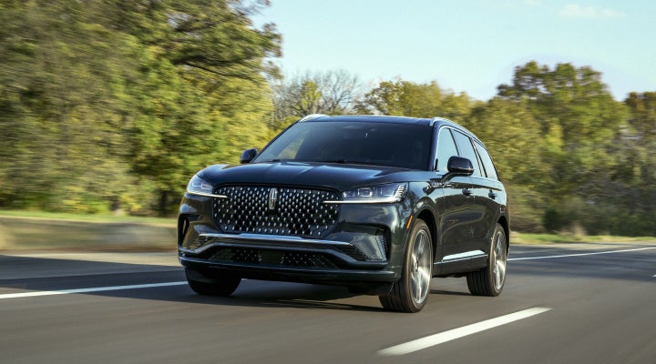 A 2026 Lincoln Black Label™ Aviator® SUV is being driven down a road lined with trees. | LaFontaine Lincoln Grand Blanc in Flint MI