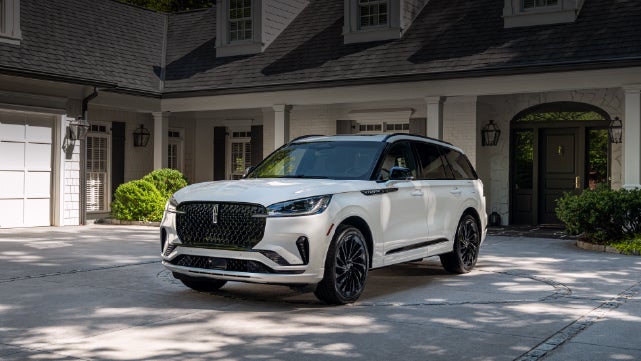 A white 2026 Lincoln Aviator® SUV is parked in the driveway of a luxury home. | LaFontaine Lincoln Grand Blanc in Flint MI
