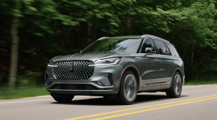 A 2027 Lincoln Aviator® SUV is being driven down a road lined with trees. | LaFontaine Lincoln Grand Blanc in Flint MI