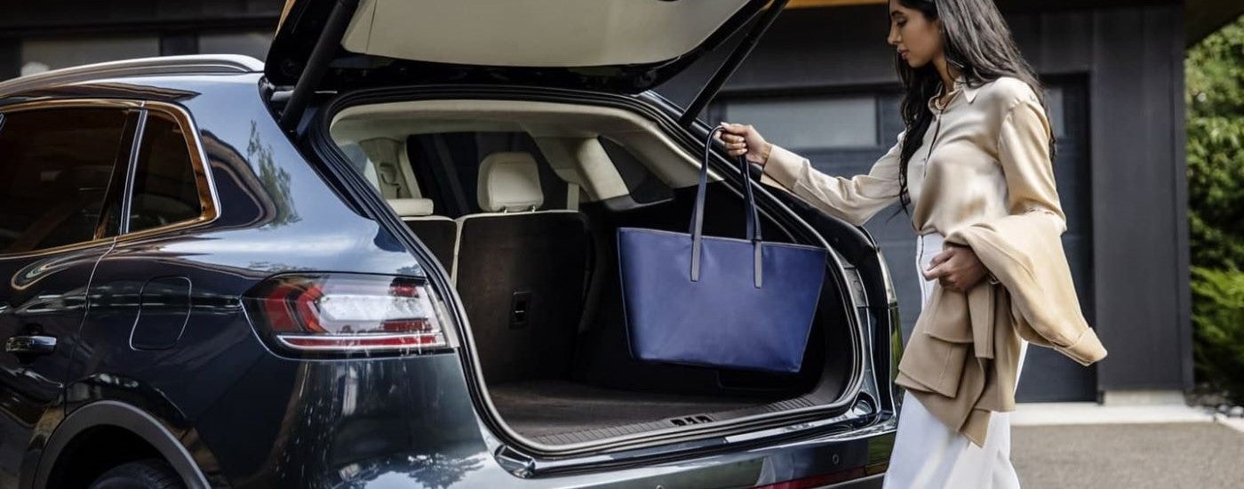 A woman putting her tote bag into a blue 2023 Lincoln Nautilus.