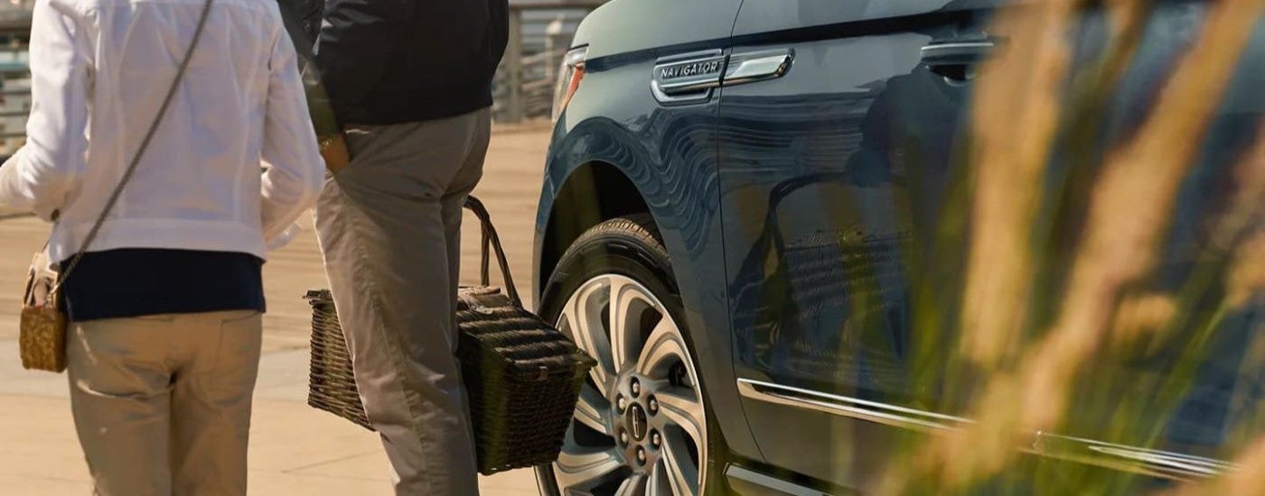 Close-up of people walking near a parked blue 2025 Lincoln Navigator for sale.