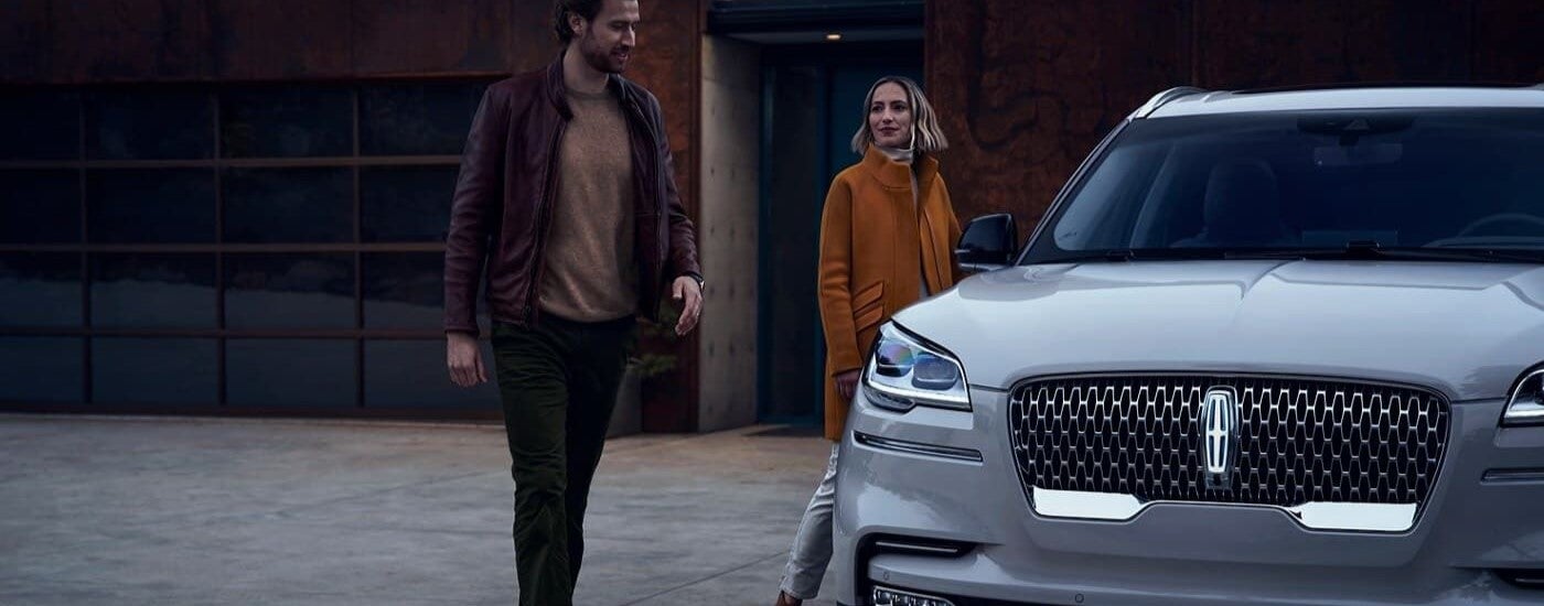 Two people walking towards a white 2023 Lincoln Aviator in a driveway